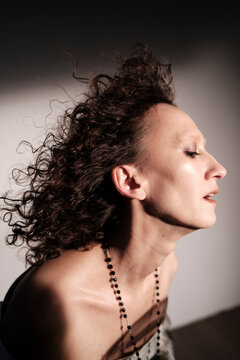 Model poses with curly hair in side profile during studio shoot