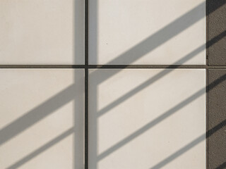 Fototapeta premium Close-up of white square tiles with diagonal shadows, creating a clean geometric background texture with minimalist style and modern design feel. 