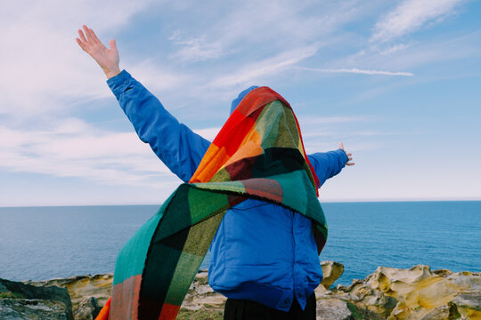 Person stands on a cliff with arms open wide by the sea