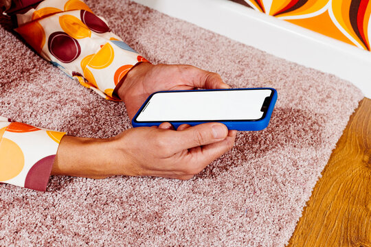 a man holds his smartphone with a blank screen lying on a carpet