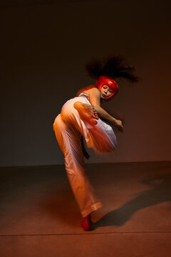 Dancer performs high kick in studio with dramatic lighting