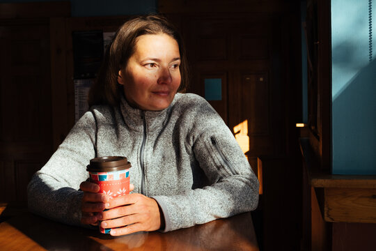 Woman sitting at table with takeaway coffee cup in sunlight