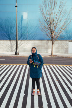 Smiling woman standing on striped crosswalk holding phone