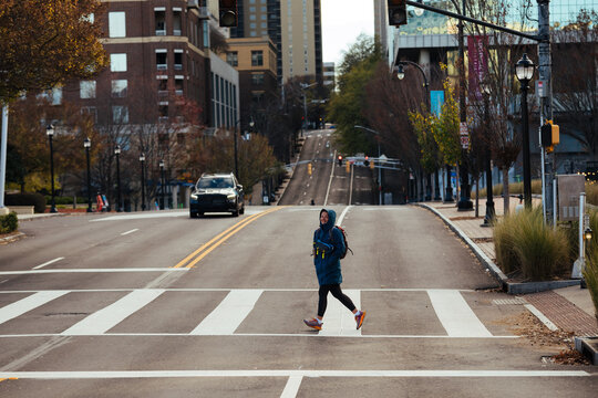 Woman crossing empty city street with backpack