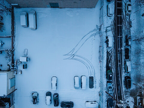 Snow-covered parking lot with tire tracks and parked cars
