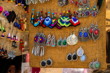 A vibrant and colorful collection of handmade earrings hanging on a corkboard display at a craft market in Brazil, showcasing a variety of unique, artisanal jewelry designs and cultural traditions