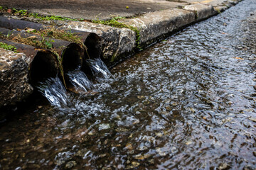 Three drainage pipes discharging water into a street gutter. A concept for urban infrastructure, stormwater management, and water pollution in Brazil.