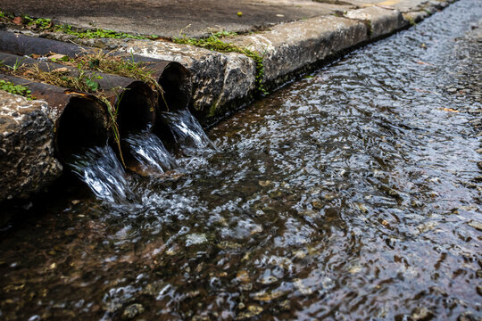 Three drainage pipes discharging water into a street gutter. A concept for urban infrastructure, stormwater management, and water pollution in Brazil.