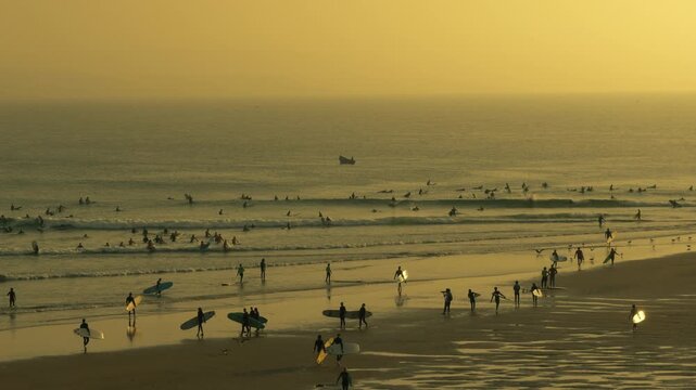 Ocean sunset at Imsouane beach in Morocco with surfers waiting for waves, cinematic coastal travel scene shot from a wide view