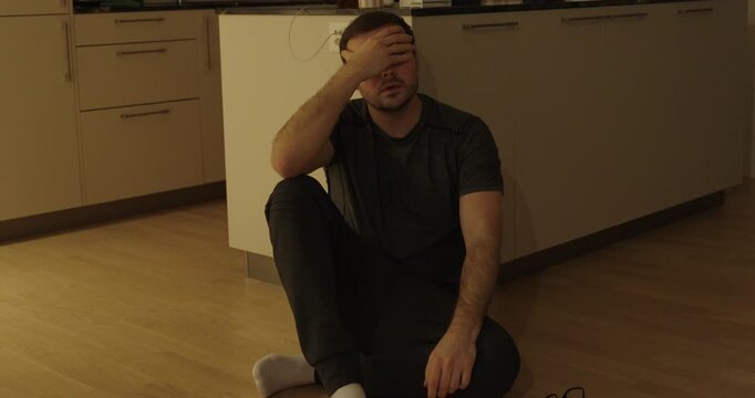 Emotional stock footage showing a man sitting on the kitchen floor in frustration, taking off his glasses in disappointment, then motivating himself to stand up and move on, symbolizing setback, self-