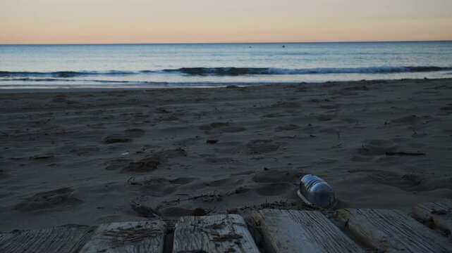 A plastic bottle on the beach, with the sea and a kayaker in the background. Slow motion and sunset. x0.5