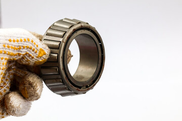 Hand in white dotted glove holding a heavy duty tapered roller bearing isolated on white background industrial mechanical part for machinery maintenance.