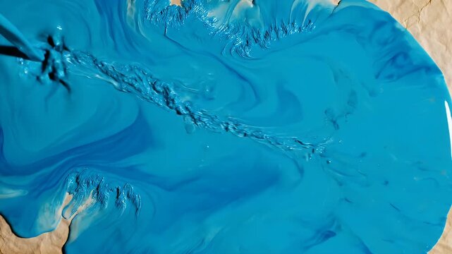 Vivid blue liquid fluidly pours onto textured, crumpled brown paper, creating abstract forms