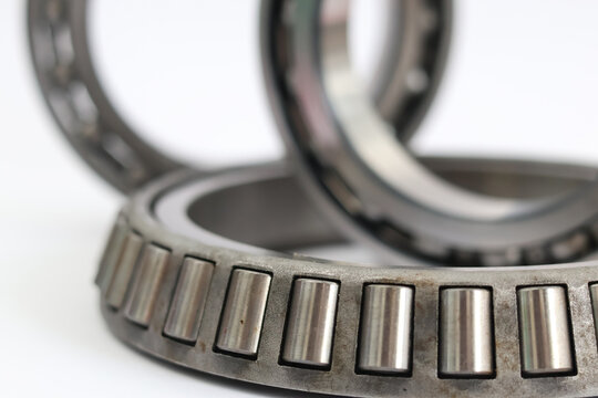 Comparison of industrial ball bearing and tapered roller bearing stacked on white background professional mechanical parts for automotive and machinery repair.