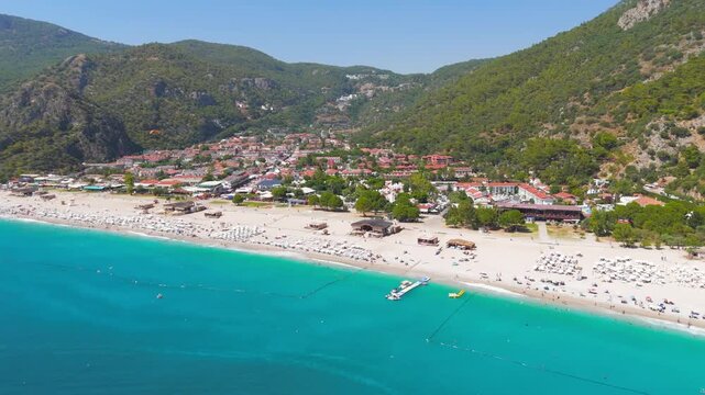 Oludeniz, Turkey. Aerial view of Oludeniz Beach infrastructure, rows of sun loungers under thatched umbrellas, people on pebble beach, beach club and clear blue water, summer. Aerial View, MasterShot