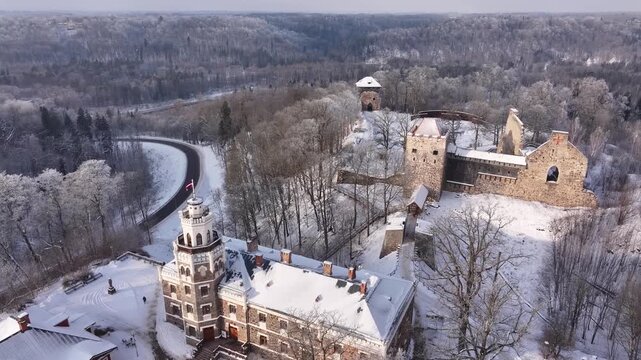 Aerial view of Sigulda s new and medieval castles in Latvia. Below, the New Castle features a rectangular shape with snow-covered roofs and ornate architecture. Behind it, the medieval castle ruins.