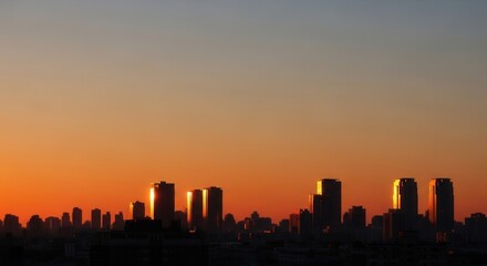 Fototapeta premium City skyline at sunrise with towering buildings reflecting golden light against a vibrant orange and blue gradient sky