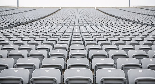 Empty stadium seating with rows of gray chairs in a large sports arena or event venue ready for spectators during daytime with bright lighting and clear sky background