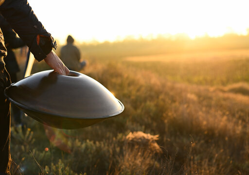 hang in the hand of a man on the background of a summer field. handpan in a golden field. A man carries a hang at dawn. hang musical instrument.