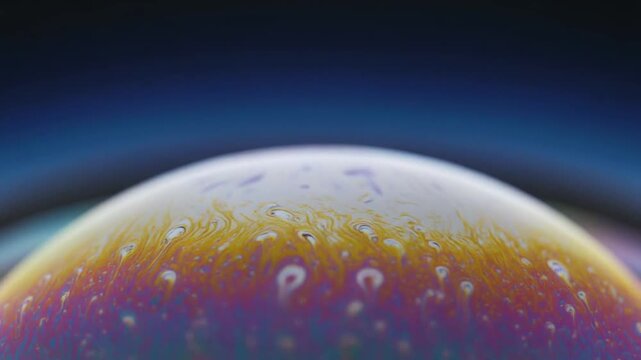 Rainbow-colored soap bubble floating in air with dark background and water droplets