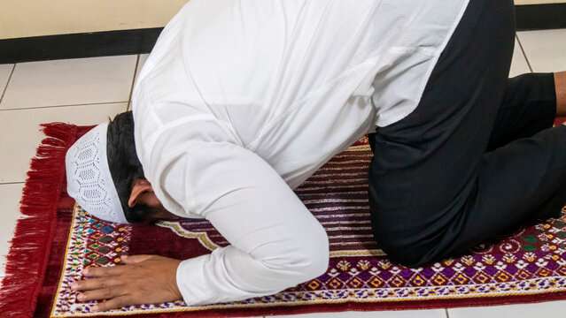 a Muslim man is praying while prostrating on a prayer mat