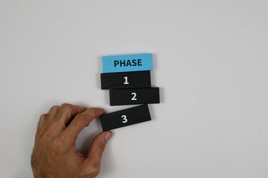 hand arranging numbered phase blocks (1, 2, 3) beneath a blue PHASE tile against an white background, symbolizing project planning and step-by-step progress.