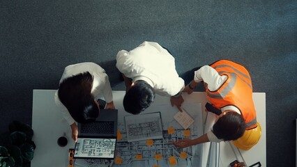 Top view of smart architect and skilled civil engineer team working together to design building construction while standing at meeting table with blueprint, equipment and safety helmet. Alimentation.