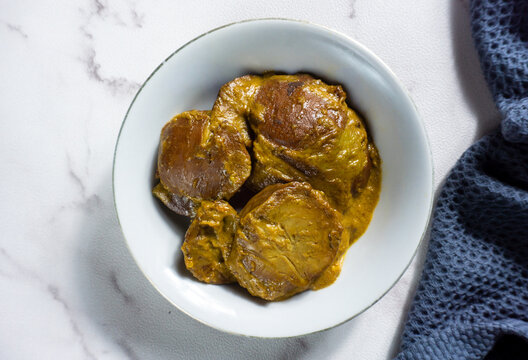 Rendang Jengkol, a traditional Indonesian dish made from jengkol beans (Archidendron jiringa). served in a white bowl with a blue napkin nearby. Flat lay 
