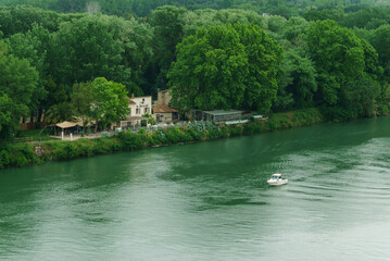 Obraz premium A small boat creates ripples on a calm river, surrounded by lush greenery and cozy cabins