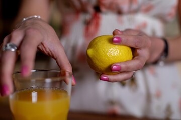 Hand holding lemon above drink, Closeup of lemon and hand preparing juice, Natural light illuminates hand and lemon during everyday juice preparation in cozy kitchen