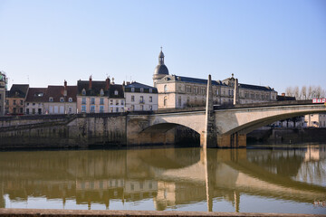 Obraz premium Traditional French architecture along the river with bridge and calm water reflections in morning light. Chalon sur Saone