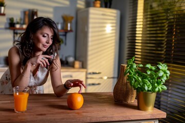 Caucasian woman reaching orange on table with thoughtful gesture, closeup of hand and fruit against warm kitchen background, moment of mindful eating and intentional selection
