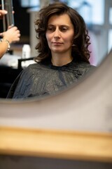 Stylish woman getting haircut, Relaxed woman seated as stylist carefully trims hair nearby, Casual scene of woman sitting calmly during professional hair cutting service