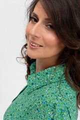 Engaging woman in green blouse, slight smile, candid threequarter pose, lifestyle coach vibe, poised body language, glossy hair, smooth skin tone, minimal background