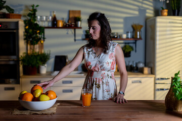 Female picks fruit from counter, Woman in kitchen selects fresh oranges, Female in comfortable kitchen environment extends hand to pick ripe oranges from wooden tabletop