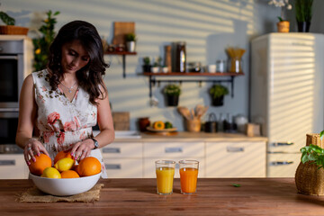 Refreshing morning beverage, Bright kitchen scene with woman pouring fresh orange juice, Morning ambiance with woman making citrus juice amid sunlight and herbal backdrop