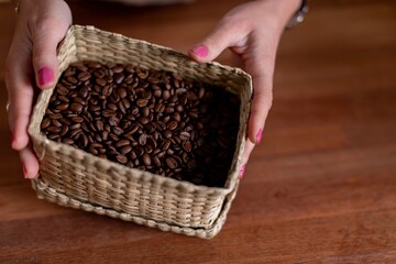 Coffee bean display, Home roaster arranging harvest in cozy setting with pink nails, Intimate depiction of hand holding glossy coffee beans on rustic wooden surface