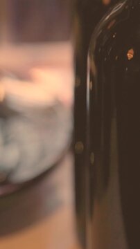 Close view of unlabeled red wine bottle fragment with dynamic wine splash inside glass decanter behind. Elegant alcohol beverage scene with motion liquid texture studio light reflections