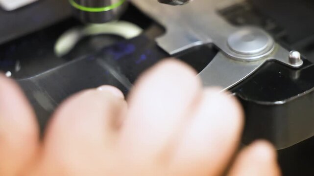 Close up laboratory video footage showing controlled movement of microscope stage while observing specimen on glass slide. Precise mechanical adjustment used in medical research diagnostics histology