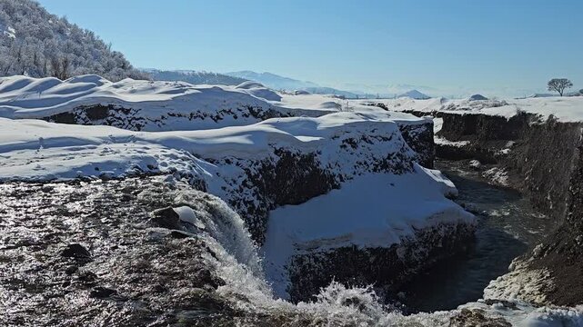 A winter waterfall drops into a deep snowy gorge, with flowing water carving through exposed dark earth under a clear blue sky.
📍Marivan, Kurdistan 