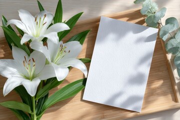 a blank white sheet of paper on a light wooden table, with shadows and a few lily flowers.