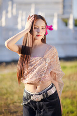 Trendy Thai fashion woman wearing a traditional Sabai paired with denim jeans at temple, reflecting...