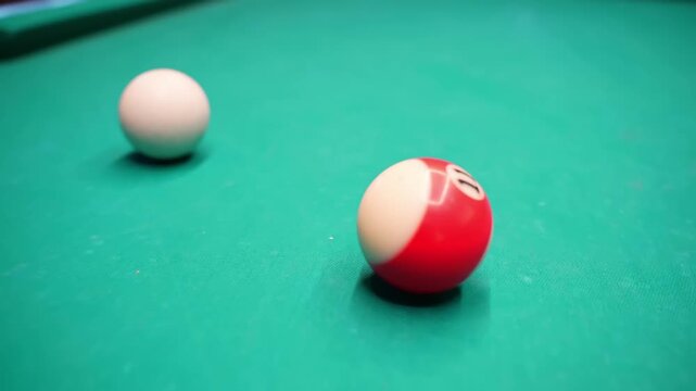 Close-up on a green pool table showing the white cue ball and a red striped ball in shallow focus, cinematic indoor bar game footage with clean copy space.