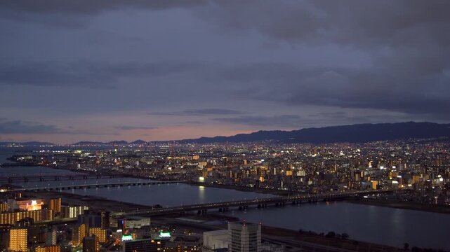 Aerial twilight view looking northwest from Osaka's Umeda Sky Building. Featuring the Yodo River, Osaka Bay, the Juso district, and the distant Mount Rokko range in winter. Filmed in Osaka, Japan