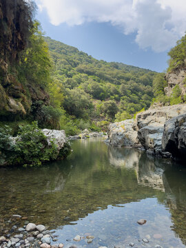 Scenic view of the transparent natural pools and rocky riverbed of Sa Stidiosa, surrounded by green Mediterranean hills in Sardinia, Italy.