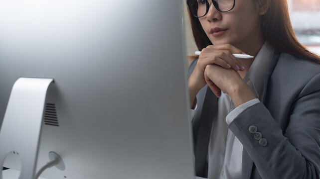Closeup, businesswoman working on desktop computer at office. Woman manager seriously looking at computer screen, thinking about problem solution. Business online meeting, planning and solution