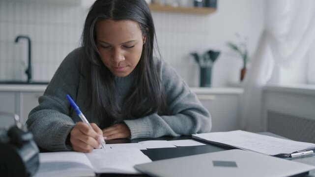 Young black woman learning online, doing homework in home workplace, portrait. African american lady writing in pad, freelance and distant education, female student practicing foreign language