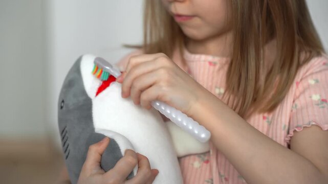 Close up of little girl brushes teeth of toy shark. Childrens hands with toothbrush. Baby milk teeth change. Oral hygiene. Health care