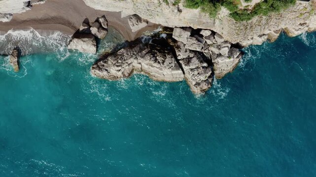 Drone Shot Highlighting Sea Coast Erosion caused by constant wave impact. Top Down Aerial View of Turquoise Sea Water Waves Crashing on Rocky Coastline Cliffs.