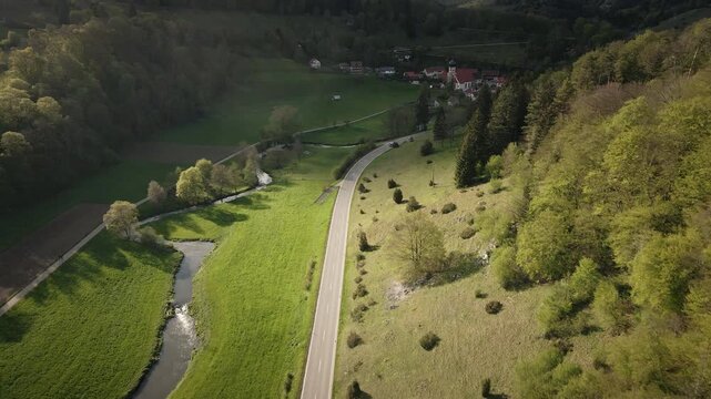 Smooth 4K UHD drone push-in flying forward following a curving country road beside the meandering Gro&szlig;e Lauter river in the Lautertal (Gro&szlig;es Lautertal), Swabian Alb, Baden-W&uuml;rttemberg, Germany.
